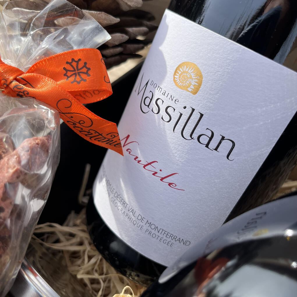Détail d’un coffret cadeau du Domaine Massillan avec la cuvée Nautile rouge, un vin bio Merlot Cabernet Sauvignon élevé 1 an en fût de chêne, présenté dans une élégante boîte noire garnie de paille naturelle, accompagné de biscuits croquants artisanaux.